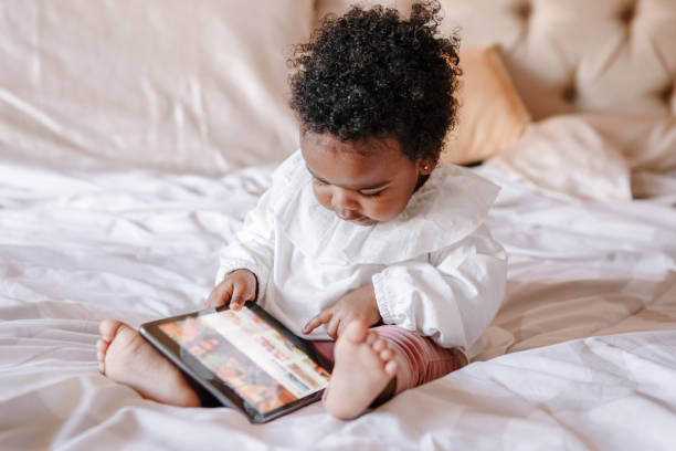 mixed race african black toddler baby girl watching cartoons on tablet. ethnic diversity. little kid child using technology. early age education development. video chat or video call. - family african ethnicity black african descent imagens e fotografias de stock