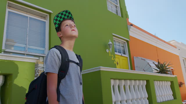 Boy tourist in Cape town Bo-Kaap Malay area, perspective of cobble stone street, colored terrace houses, laundry on line side of house.