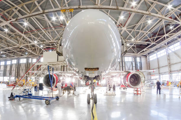 aerei sotto il tetto dell'hangar aviazione industriale in manutenzione, fuori dal cancello luce intensa. - hangar foto e immagini stock