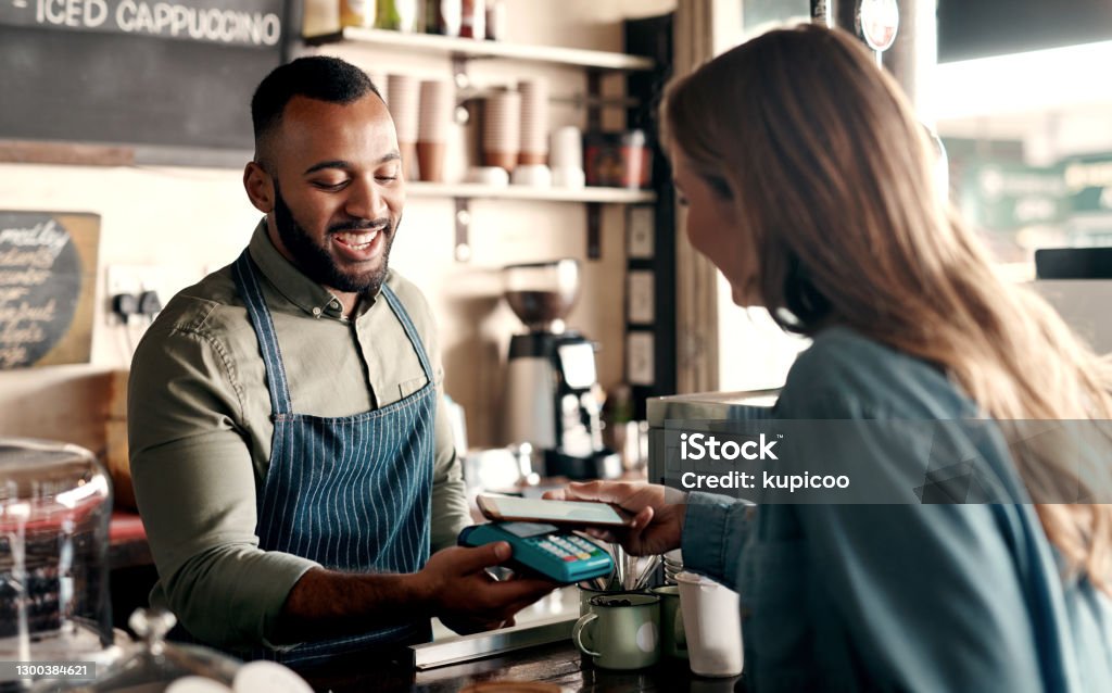 Tap-to-pay technology is so convenient Shot of a young man accepting a digital payment from a customer in a cafe Paying Stock Photo