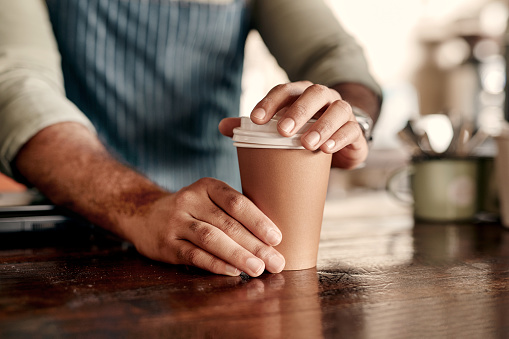 Closeup shot of a barista sealing a lid on a coffee cup in a cafe