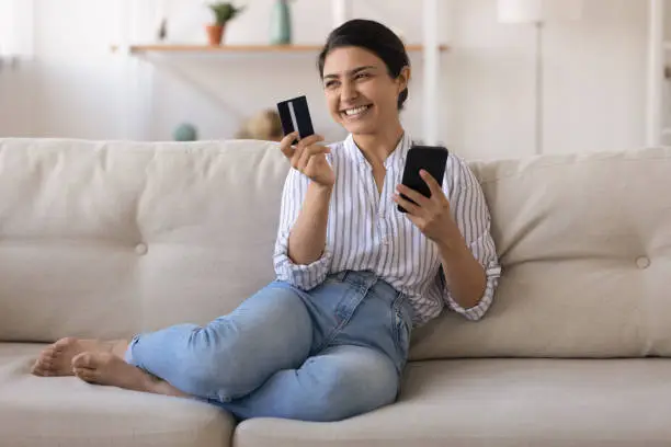 Excited indian female bank customer use phone to make easy secure payments online in convenient app. Glad mixed race lady dream of spending bonus cashback received on credit card for internet paying