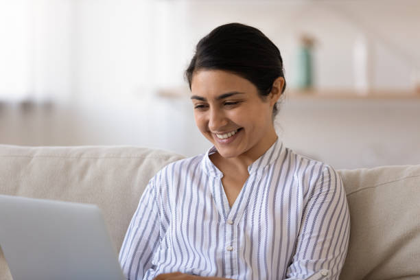istock Millennial indian woman sit on couch use laptop install software 1300386346