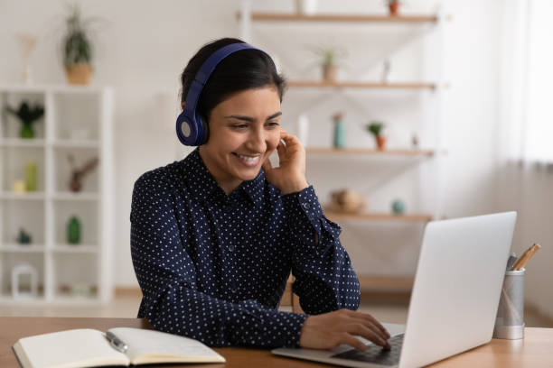 istock Indian female in headset sit by laptop choose course online 1300386390