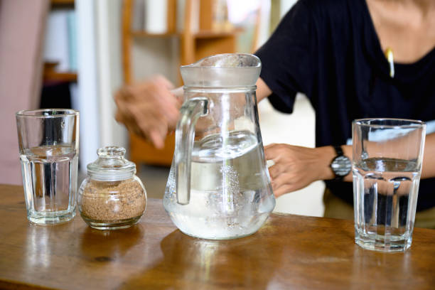 Unrecognizable woman picking up jug filled withcold water, two drinking glasses are on table, Nikon Z7