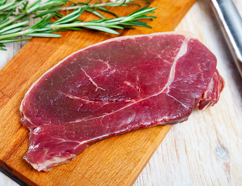 Ingredients for cooking. Slice of fresh raw horse meat fillet on wooden table with rosemary