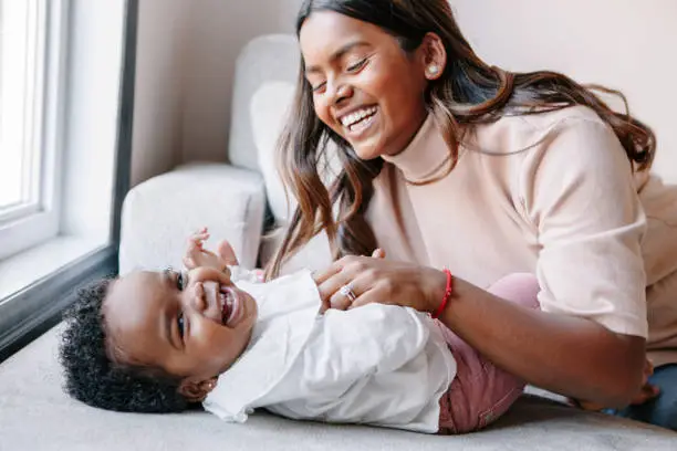 Photo of Happy smiling laughing Indian mother playing with black baby girl daughter. Family mixed race people mom and a kid together hugging at home. Authentic candid lifestyle with infant kid child.