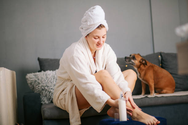 istock Young woman sitting on sofa and applying moisturizing cream on her legs 1300395960