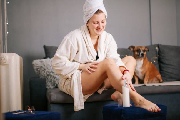 istock Young woman sitting on sofa and applying moisturizing cream on her legs 1300396038