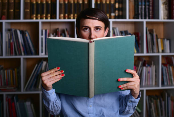 istock Young woman holding book in library 1300397111