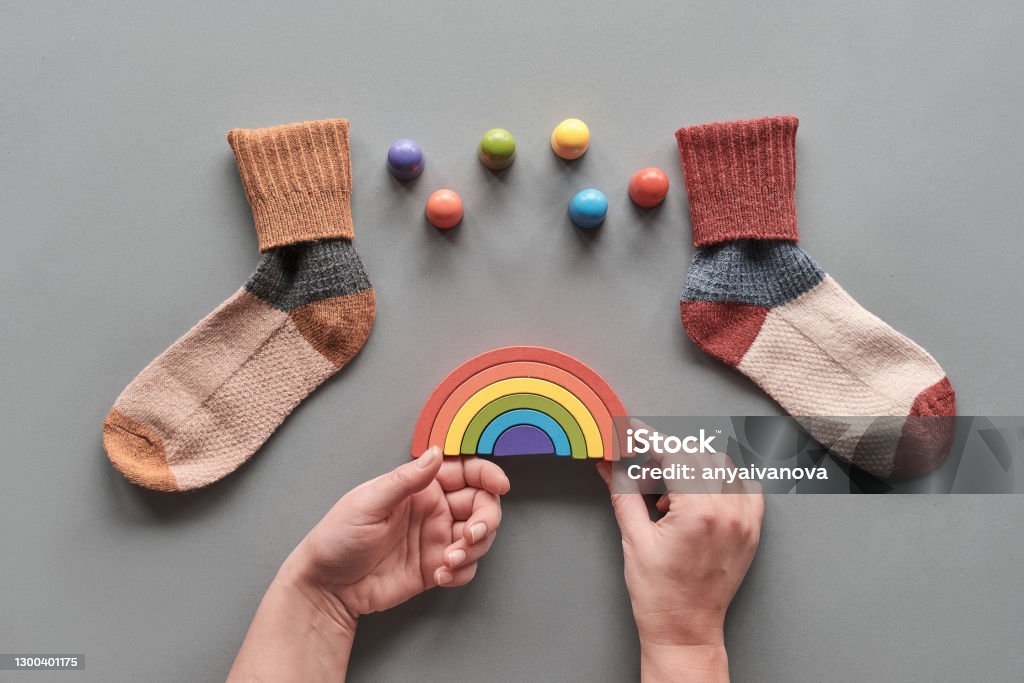 Odd Socks Day.Mismatched socks, wooden rainbow and toy figures. Social initiative against bullying in school or workplace. Design for anti-bullying campaign visual Odd Socks Day. Mismatched socks, hands holding wooden rainbow, toy figures. Social initiative against bullying in school or workplace. Design for anti-bullying campaign poster or cards. Above Stock Photo