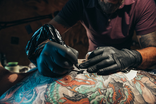 Shot of a tattoo artist hands while tattooing mans back