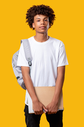 Smart black young male. Student lifestyle. Confident african teenager with notebook backpack. Looking at camera isolated on orange. Knowledge and skills. Advertising background