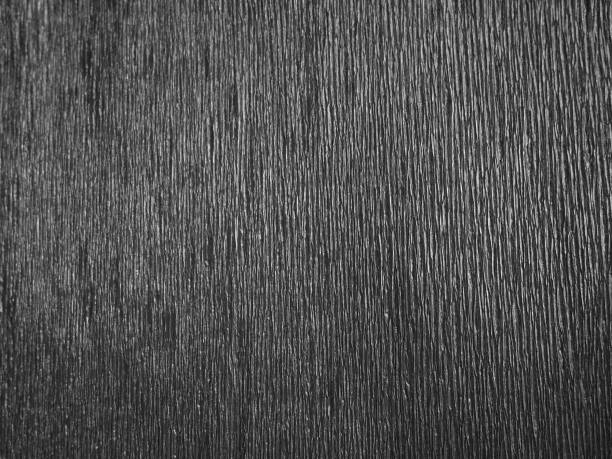 istock Black or gray corrugated paper. Uneven surface. Abstract monochrome background. Wavy edges of the paper sheet. Lighting gradient. Corrugated texture. 1300410801