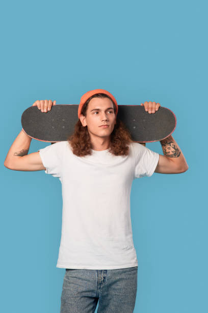 istock Young adult guy holding skateboard behind head 1300410904