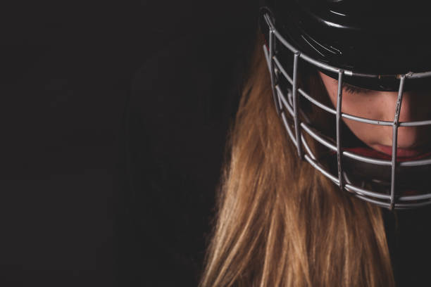Close up of female hockey player with helmet and mask, wearing black equipment on black background