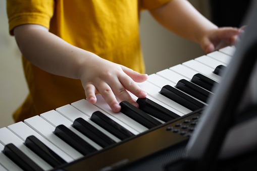 Child's hands on the synthesizer's keyboard. Toddler learning how to play piano. Small fingers pressing on the keys closeup. Early development and education concept