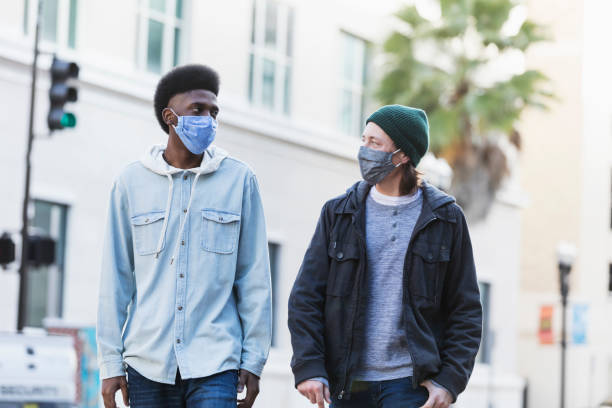 istock Two young men walking in city, wearing face masks 1300419725