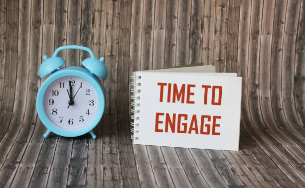 istock Text, the word Time To Engage is written in a notebook lying on a wooden table with an alarm clock. Business concept 1300436708