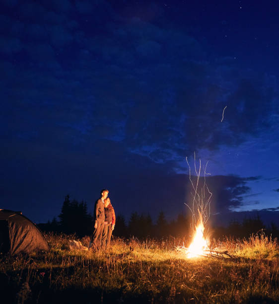 istock Young couple standing near campfire under beautiful night sky. 1300436894