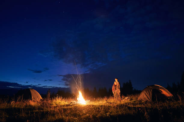 istock Young couple standing near campfire under beautiful night sky. 1300436902