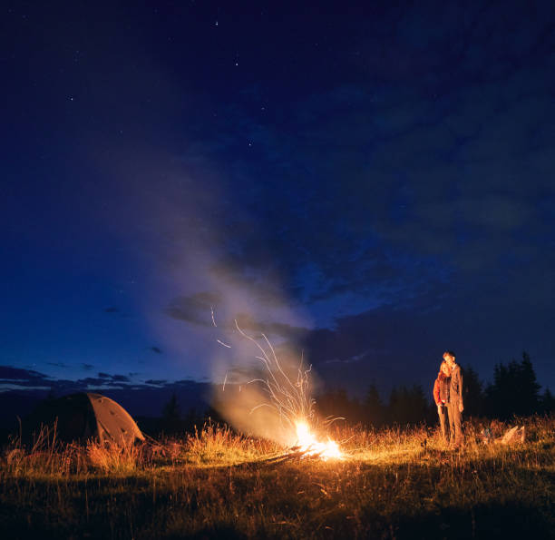 istock Young couple standing near campfire under beautiful night sky. 1300436903
