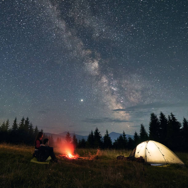 istock Young couple sitting near campfire under beautiful starry sky. 1300436917