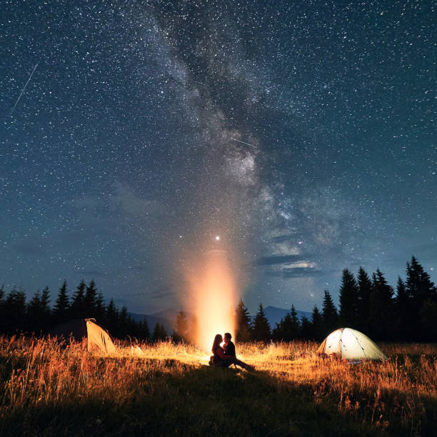istock Young couple sitting near campfire under beautiful starry sky. 1300436923