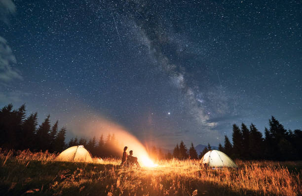 istock Young couple sitting near campfire under beautiful starry sky. 1300436925