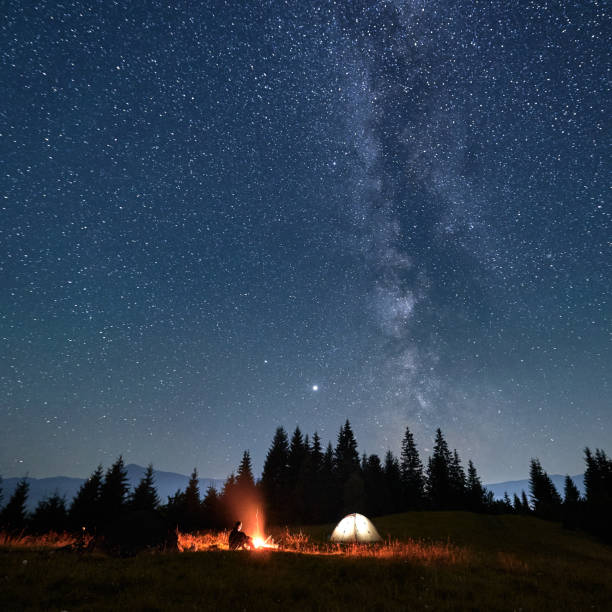 istock Hiker sitting near campfire under night starry sky. 1300436928
