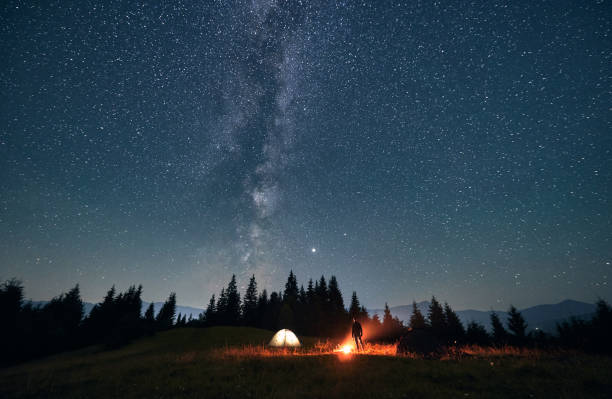 istock Hiker standing near campfire under night starry sky. 1300436933