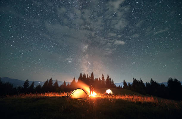 istock Hikers standing near campfire under beautiful starry sky. 1300436934