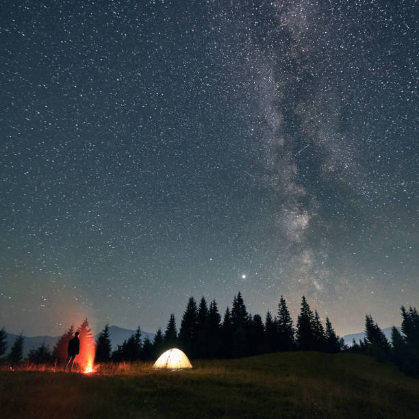 istock Hiker standing near campfire under night starry sky. 1300436940