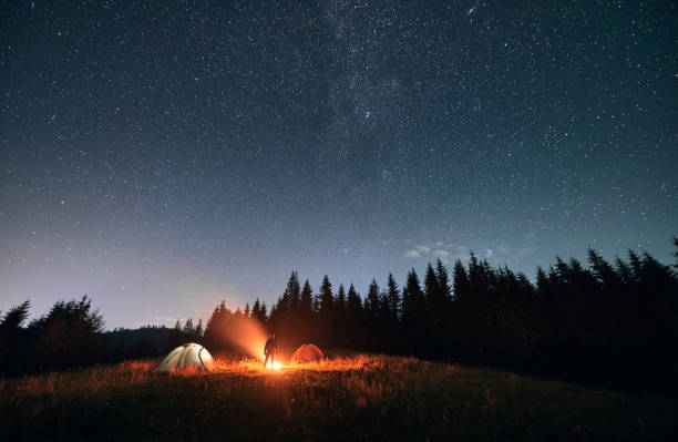 istock Hiker standing near campfire under night starry sky. 1300436959