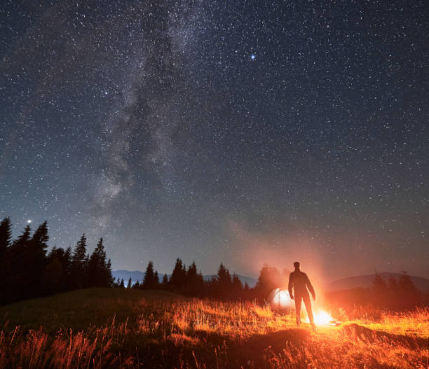 istock Hiker standing near campfire under night starry sky. 1300436971