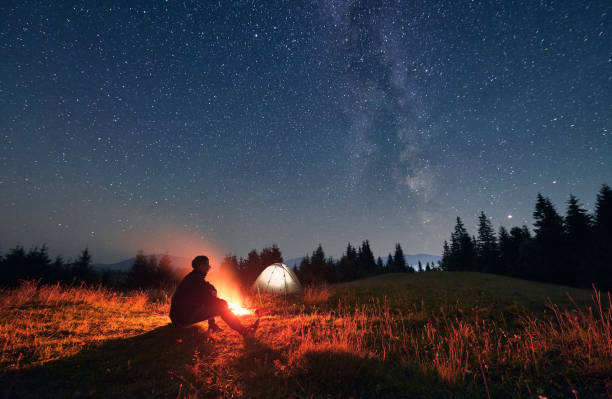 istock Hiker sitting near campfire under night starry sky. 1300436986