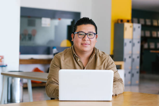 homme latin de taille plus travaillant sur l’ordinateur portatif dans le bureau dans la ville de mexico - mexican ethnicity photos et images de collection