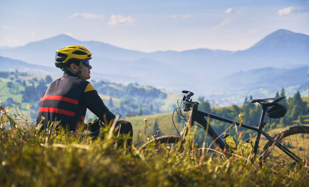 istock Man cyclist sitting on grass and looking at mountains. 1300438697