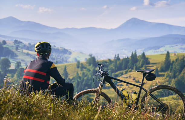 istock Man cyclist sitting on grass and looking at mountains. 1300438704