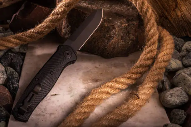 Photo of The reverse side of the knife with a clip on the background of stones and rope. Photo of a knife with a great depth of field.