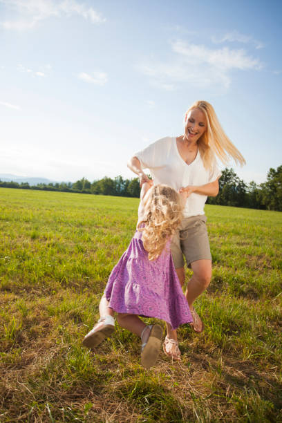 Mother spinning her girl. Having fun together in nature. Evening sun and lens flare.