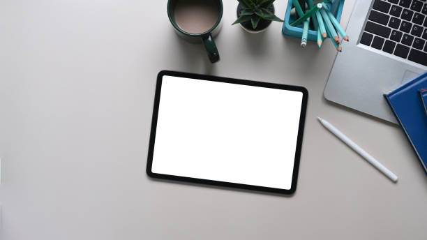 istock Mock up digital tablet with empty screen, laptop, stationery and coffee cup on white table. Top view. 1300443299