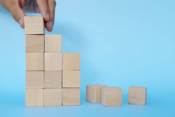 istock Hand putting together broken or fallen building blocks in blue background. Recovery, hardwork and rebuilding concept. 1300445117