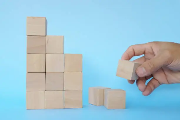 Hand putting together broken or fallen building blocks in blue background. Recovery, hardwork and rebuilding concept.