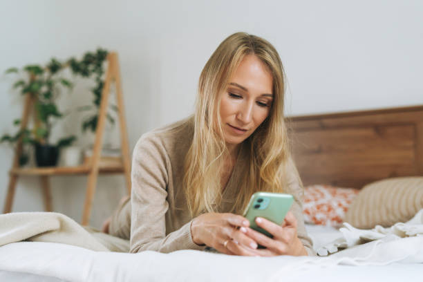 istock Beautiful blonde young woman using mobile on bed at home 1300446507