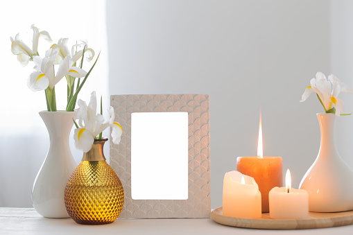 white frame, burning candles and flowers on shelf on white background