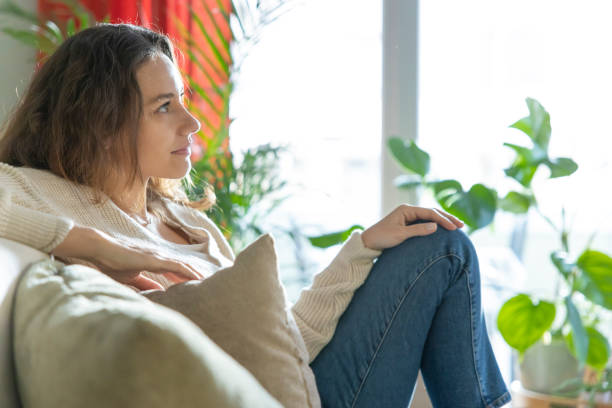 istock Smiling young woman sitting on sofa and looking away 1300449605