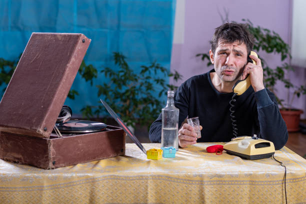 孤独な男はパティフォンとテーブルに座って、アルコールを飲み、電話で話します - eastern european caucasian one person alcoholism ストックフォトと画像