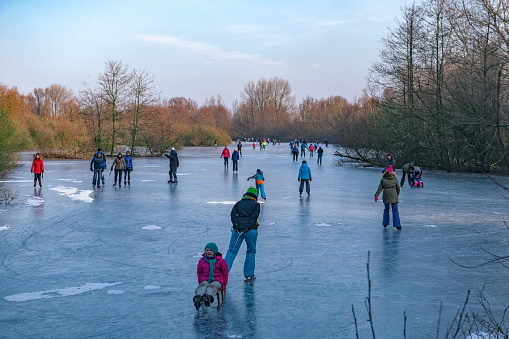 People ice skating on a frozen lake next to the river IJssel in Holland during a beautiful winter day winter. People are enjoying this typical Dutch winter activity.