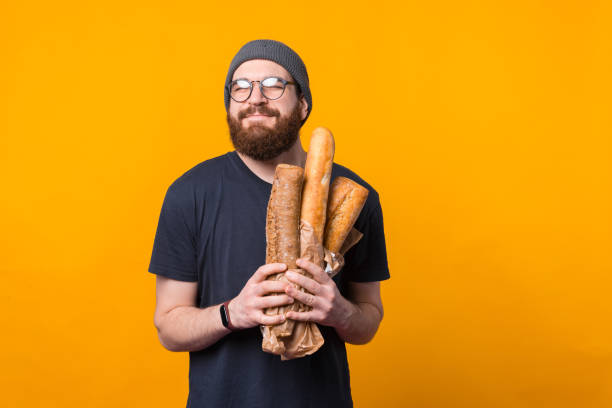 Photo of bearded hipster man holding fresh baked breads over yellow background stock photo